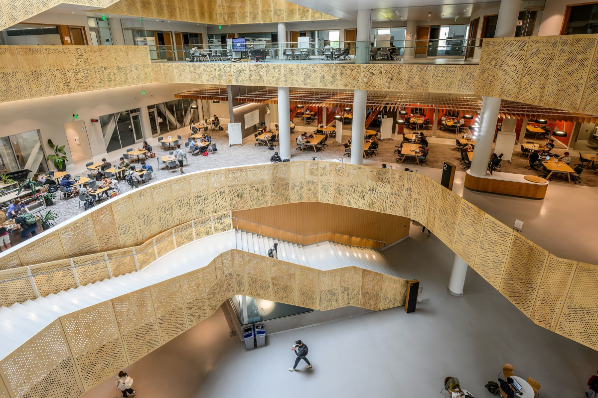 Pale yellow staircases and indoor atrium of CDIS building. Students fill tables on each floor.